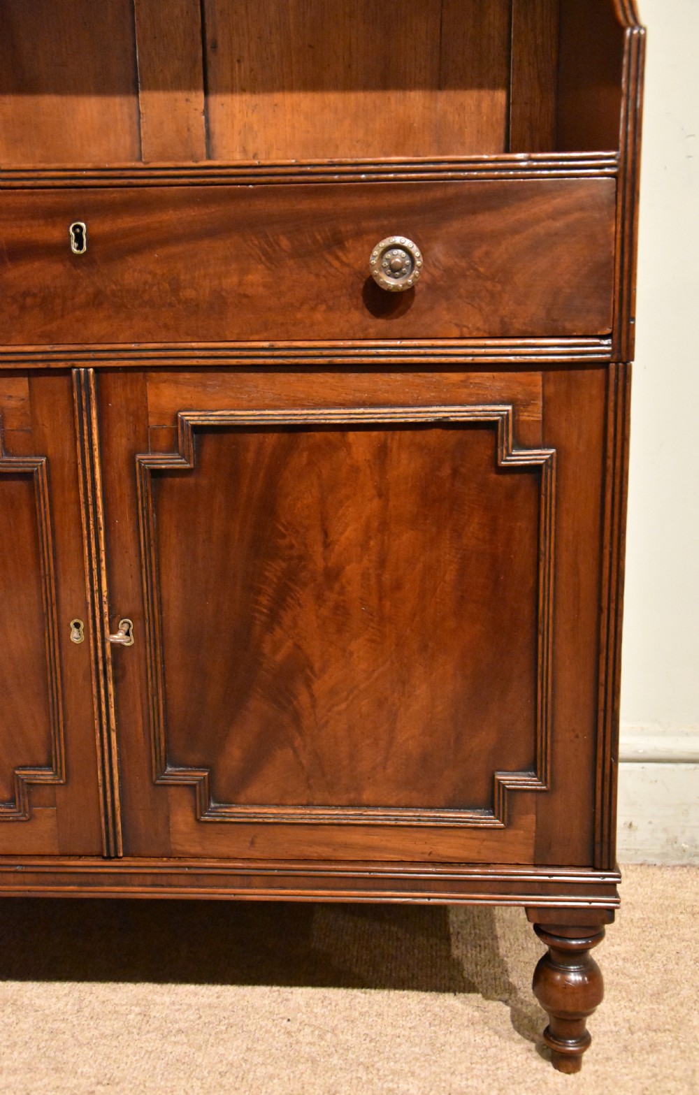 A Regency period mahogany waterfall bookcase featuring graduated open shelves, a single drawer, two lower cabinet doors, and turned feet. View VII