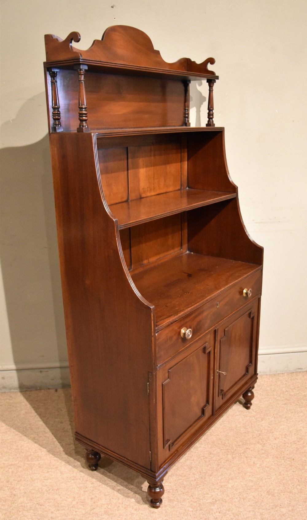 A Regency period mahogany waterfall bookcase featuring graduated open shelves, a single drawer, two lower cabinet doors, and turned feet. View VIII