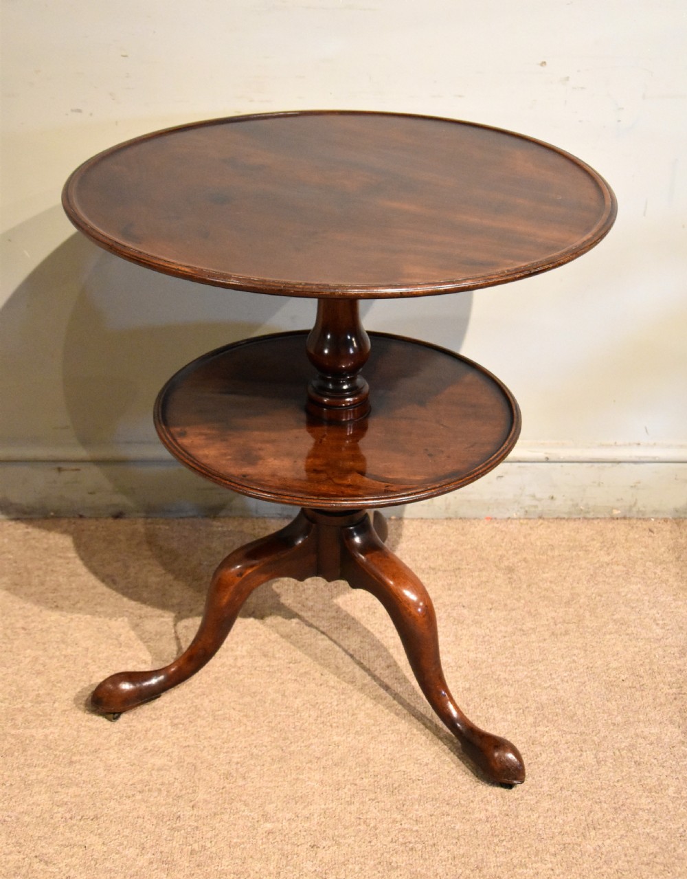 A George III mahogany two-tier tripod table featuring two circular trays supported by a central turned baluster stem and three cabriole legs ending in pad feet.