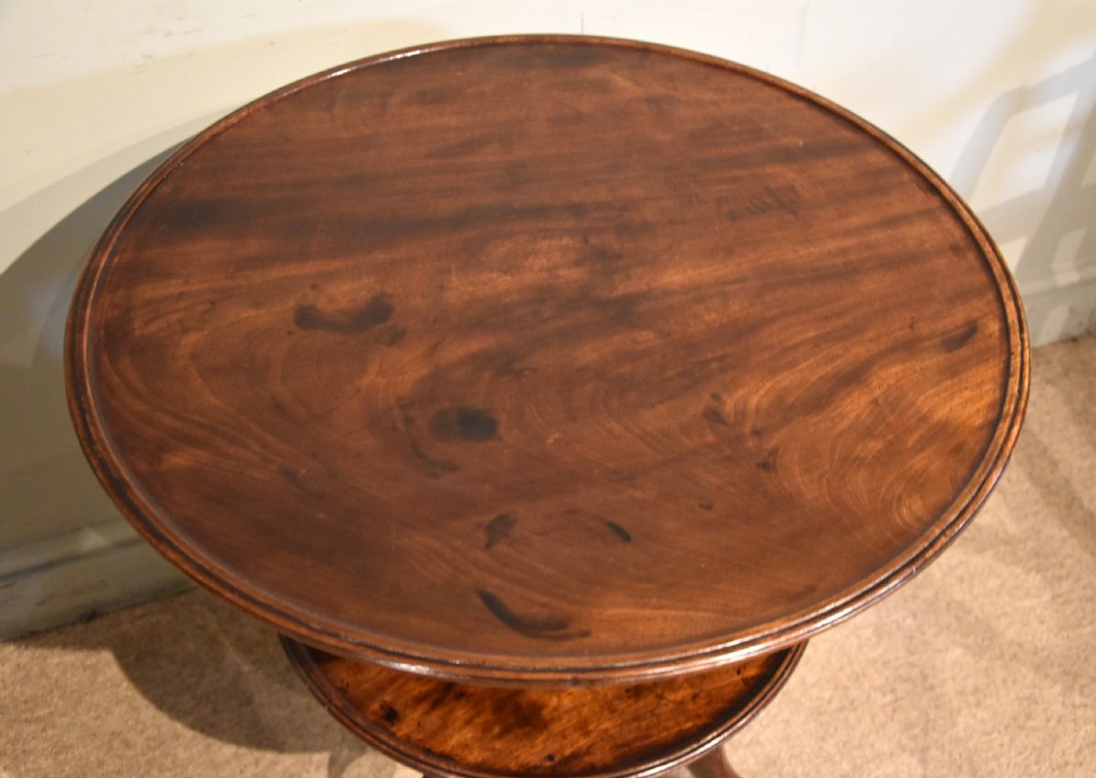A George III mahogany two-tier tripod table featuring two circular trays supported by a central turned baluster stem and three cabriole legs ending in pad feet. View V
