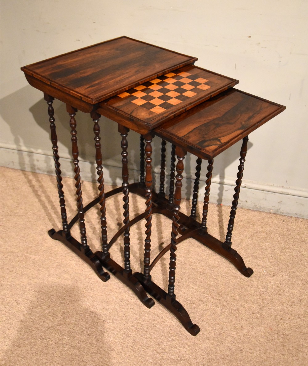 A set of three nested Regency rosewood occasional tables featuring barley twist legs, curved stretchers, and an inlaid chessboard top on the middle table.