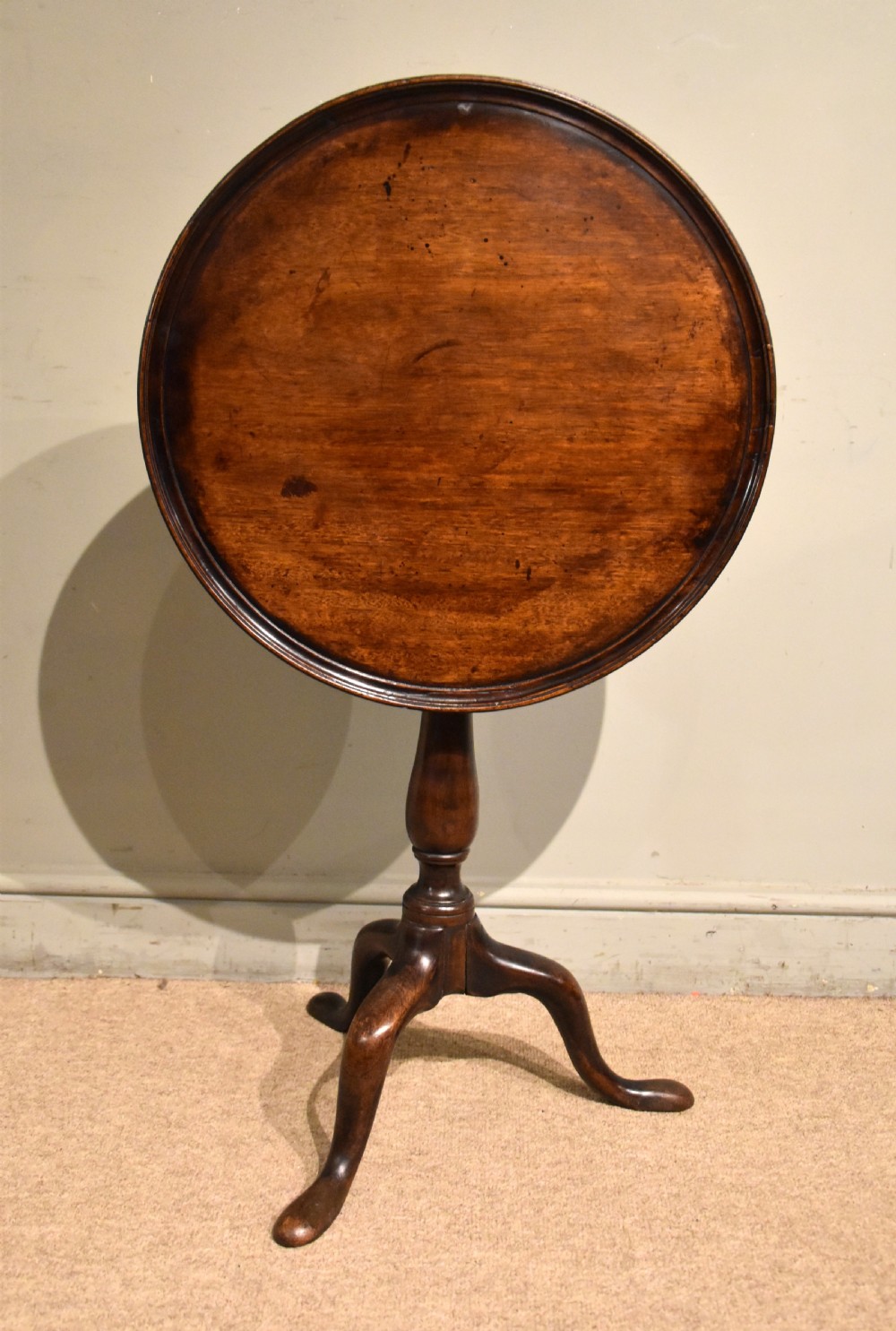 A George III mahogany wine table featuring a circular tilt top surface mounted on a turned pedestal stem and tripod legs.