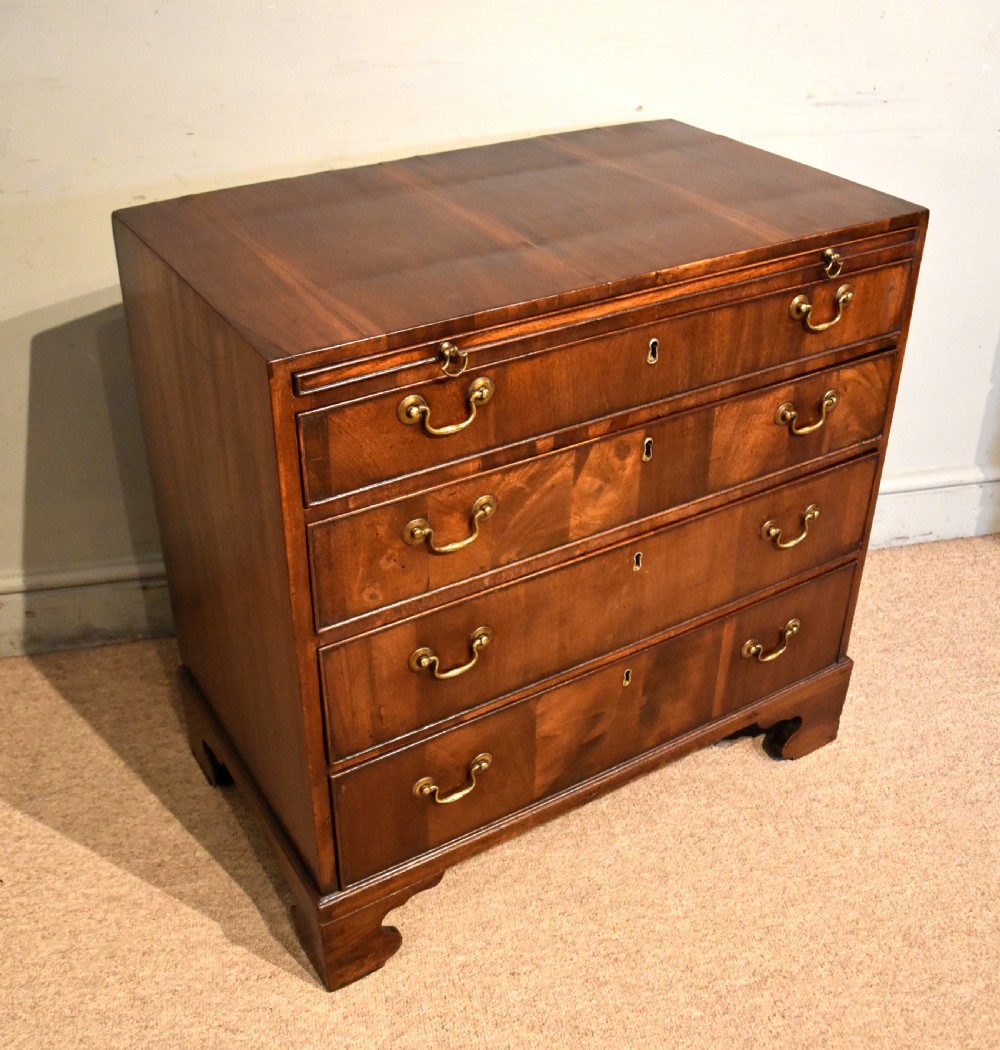 A George III walnut veneered chest of drawers with four graduated drawers, brass handles, and bracket feet. View VI