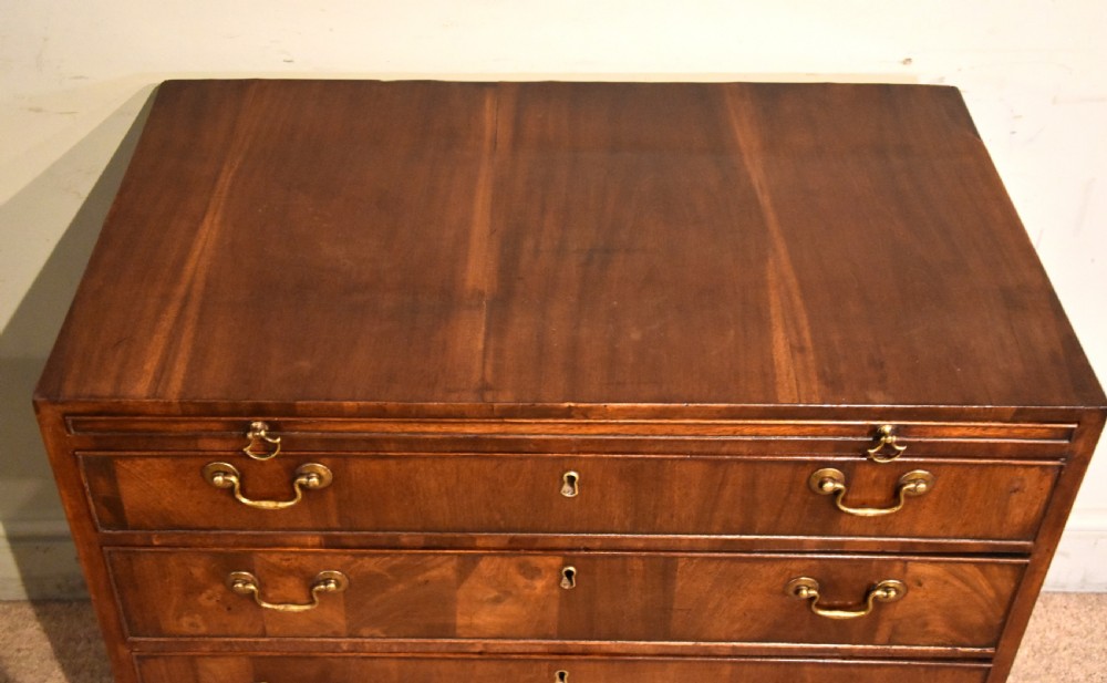 A George III walnut veneered chest of drawers with four graduated drawers, brass handles, and bracket feet. View VIII