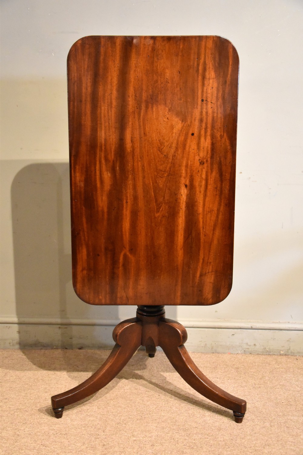 A William IV tilt-top mahogany table with a rich flame veneer rectangular top displayed upright on a turned tripod pedestal base.