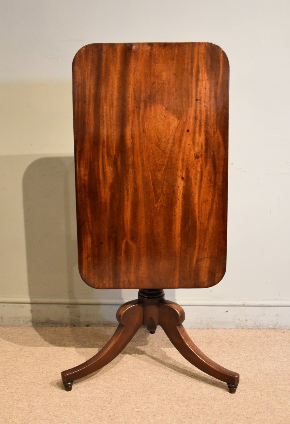 A William IV tilt-top mahogany table with a rich flame veneer rectangular top displayed upright on a turned tripod pedestal base. View II