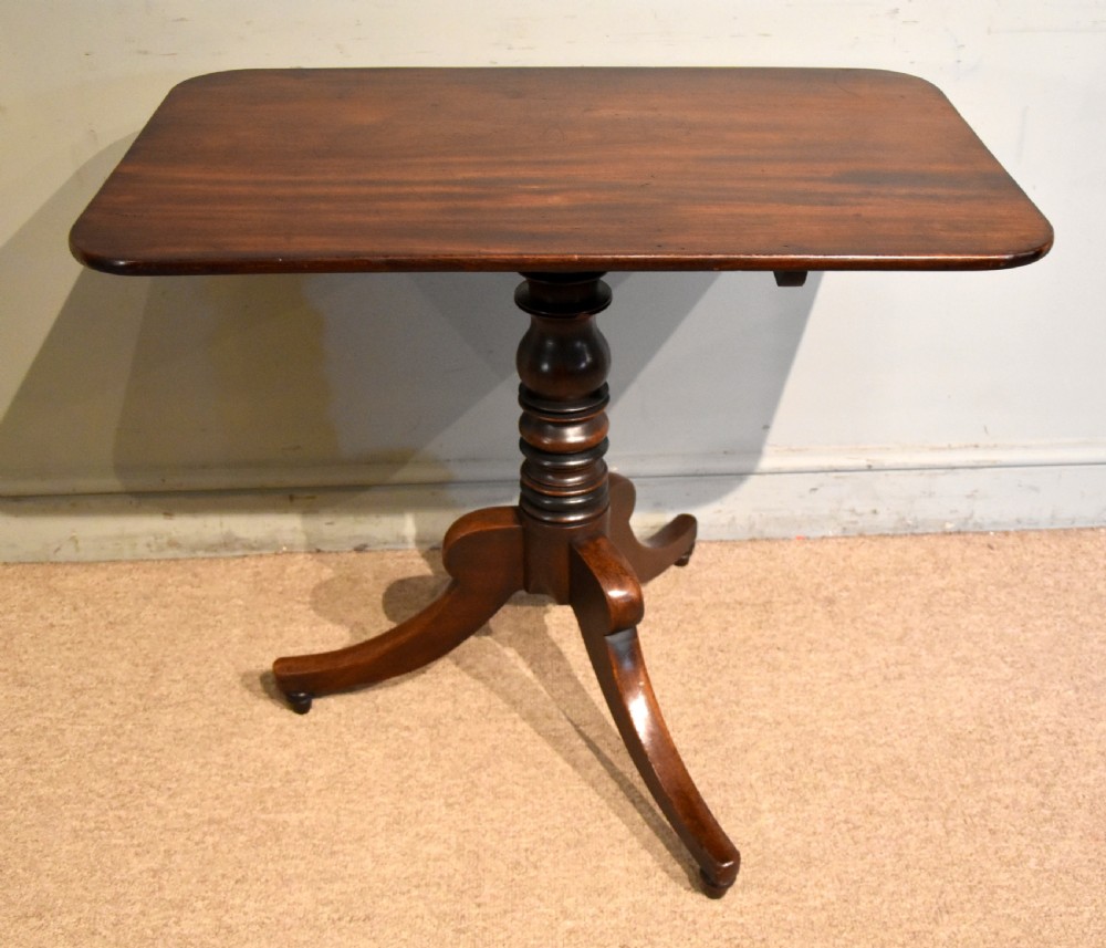 A William IV tilt-top mahogany table with a rich flame veneer rectangular top displayed upright on a turned tripod pedestal base. View IV