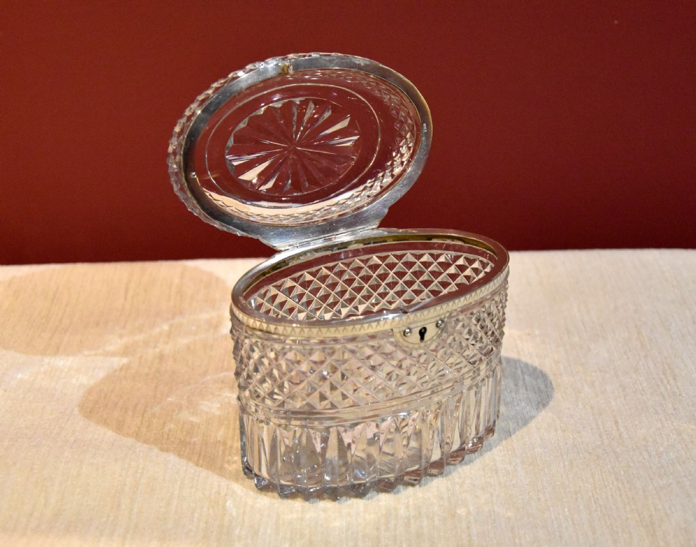 An oval cut glass Georgian tea caddy featuring diamond faceting, a hinged lid, and a silver lock plate with keyhole. View III