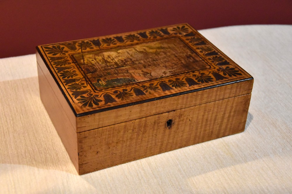 A rectangular 19th-century sycamore wood box featuring a printed architectural scene on the lid surrounded by a stylized leaf border and a keyhole on the front. View II