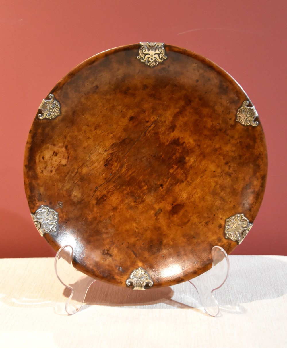 A circular shallow bowl carved from figured brown burr wood, featuring six chased silver mounts positioned around the rim.
