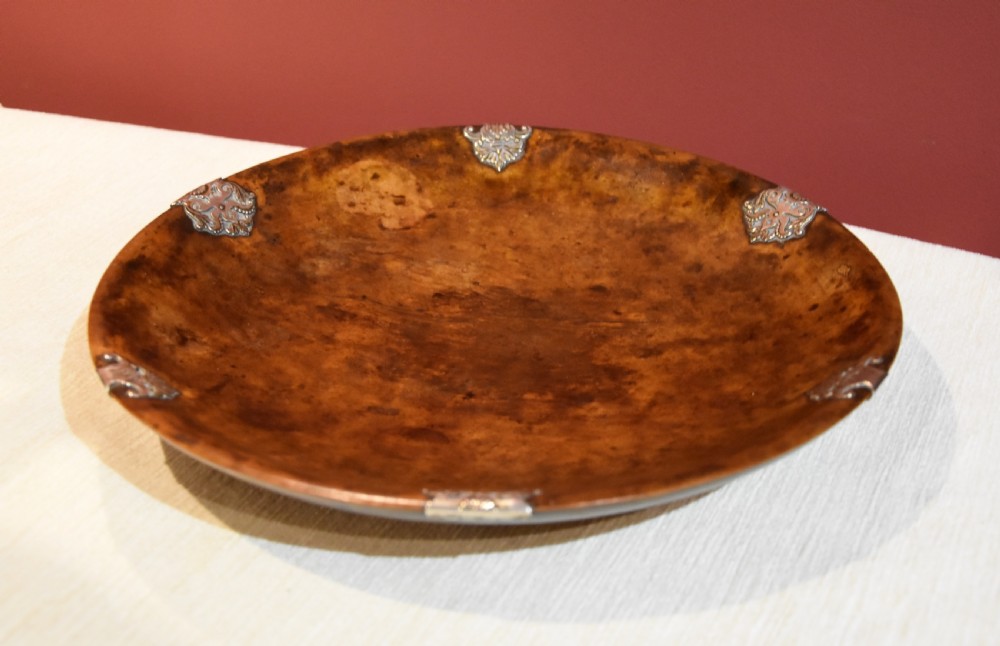 A circular shallow bowl carved from figured brown burr wood, featuring six chased silver mounts positioned around the rim. View VI