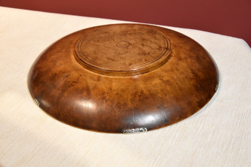 A circular shallow bowl carved from figured brown burr wood, featuring six chased silver mounts positioned around the rim. View VII