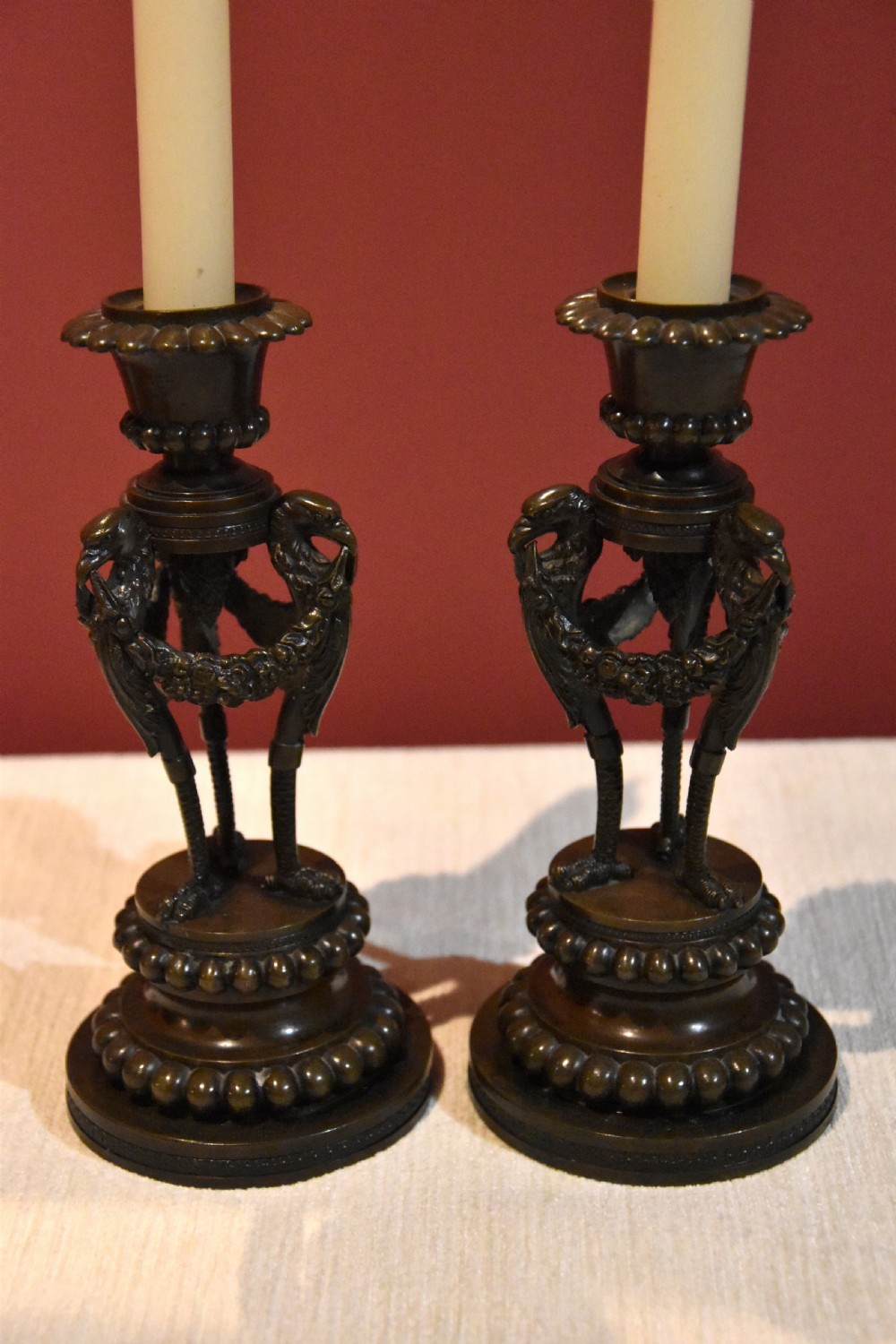 A pair of dark patinated bronze Regency candlesticks featuring detailed bird leg supports, draped floral garlands, and beaded circular bases.