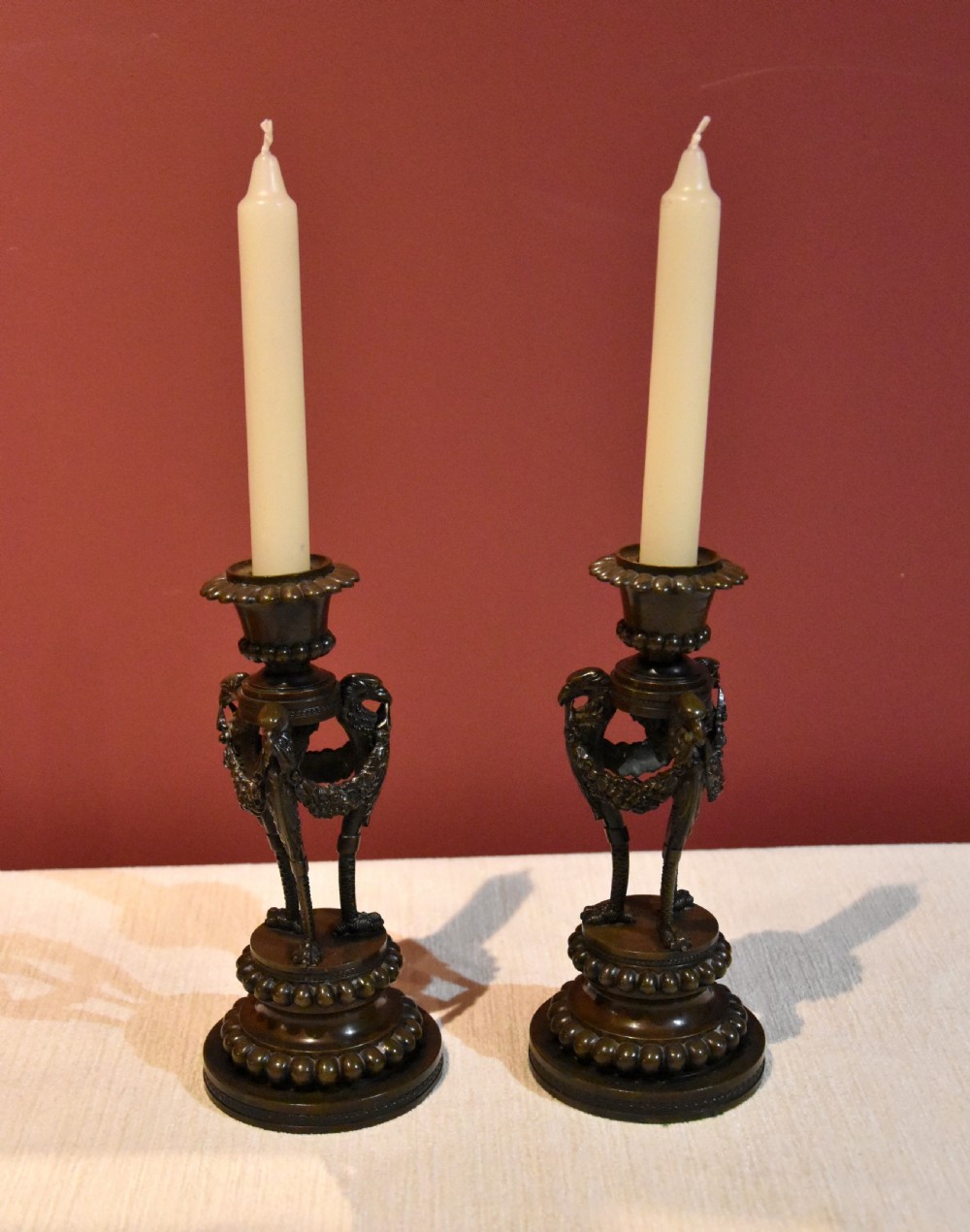 A pair of dark patinated bronze Regency candlesticks featuring detailed bird leg supports, draped floral garlands, and beaded circular bases. View II