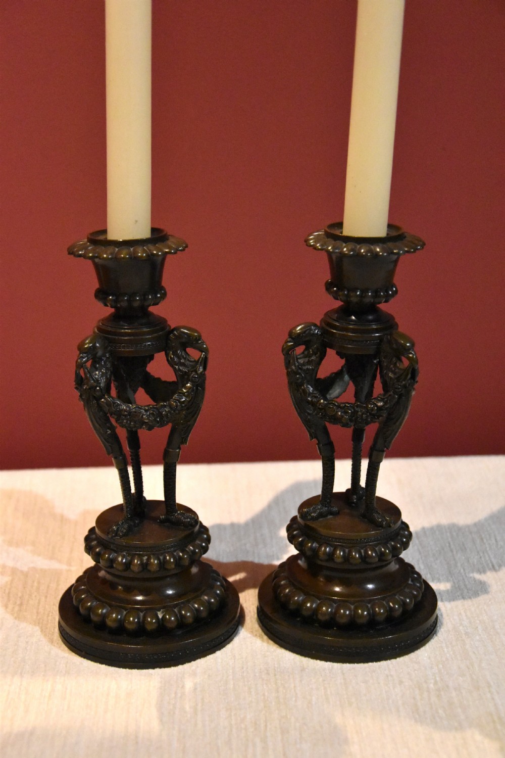 A pair of dark patinated bronze Regency candlesticks featuring detailed bird leg supports, draped floral garlands, and beaded circular bases. View III