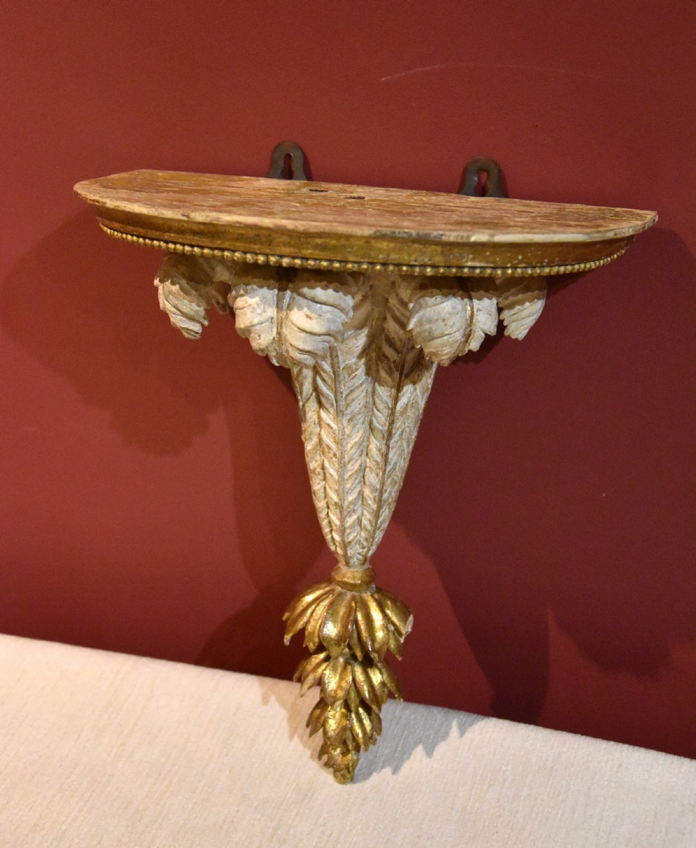 An 18th-century carved wall bracket featuring a semicircular gilded top shelf with beaded molding above a tapered white body with leaf carving and a drop leaf finial. View III