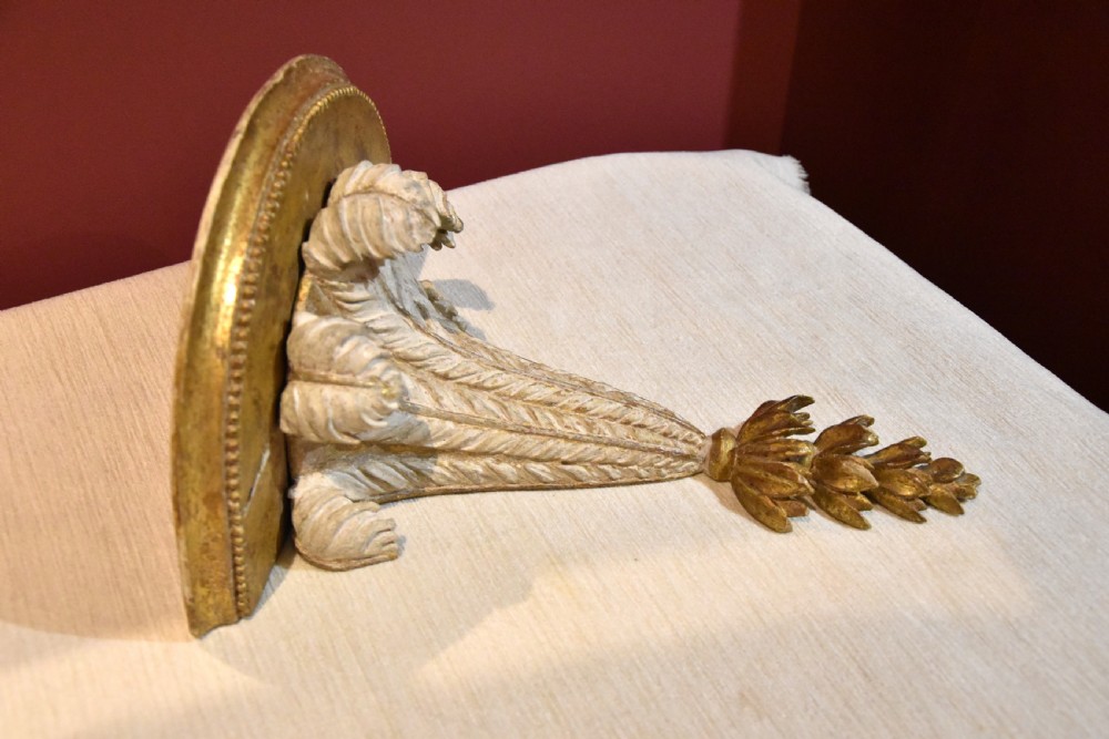 An 18th-century carved wall bracket featuring a semicircular gilded top shelf with beaded molding above a tapered white body with leaf carving and a drop leaf finial. View IV
