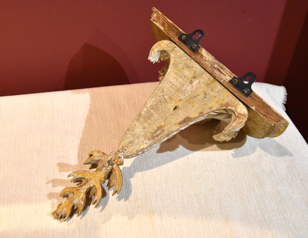 An 18th-century carved wall bracket featuring a semicircular gilded top shelf with beaded molding above a tapered white body with leaf carving and a drop leaf finial. View VII