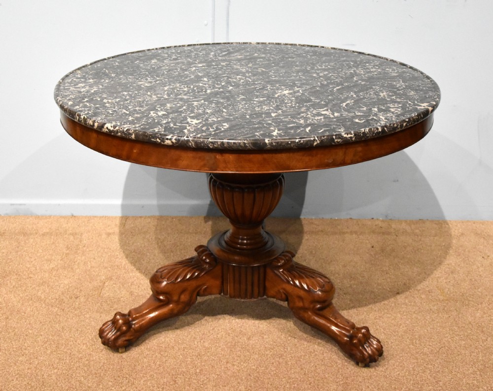 A 19th-century French mahogany gueridon table featuring a circular dark marble top supported by a reeded pedestal stem and carved triform base with paw feet.