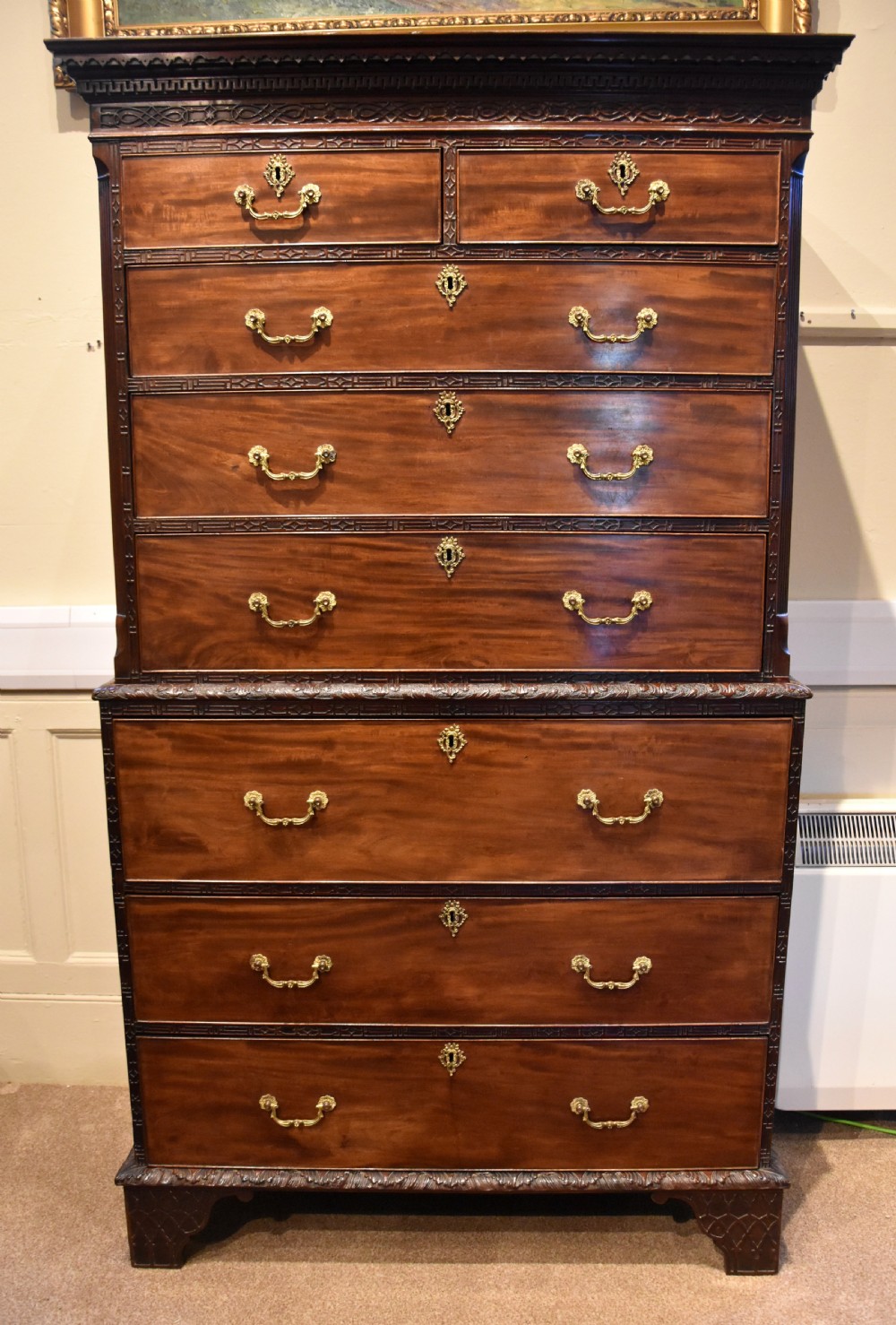 An eighteenth-century carved mahogany chest on chest featuring geometric fretwork mouldings, brass swan-neck handles, and carved bracket feet.