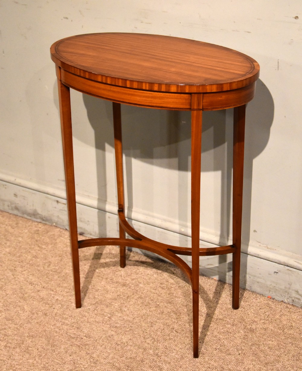 An oval Sheraton Revival occasional table crafted from satinwood with crossbanded border inlay, slender tapered legs, and a curved X-frame stretcher. View II