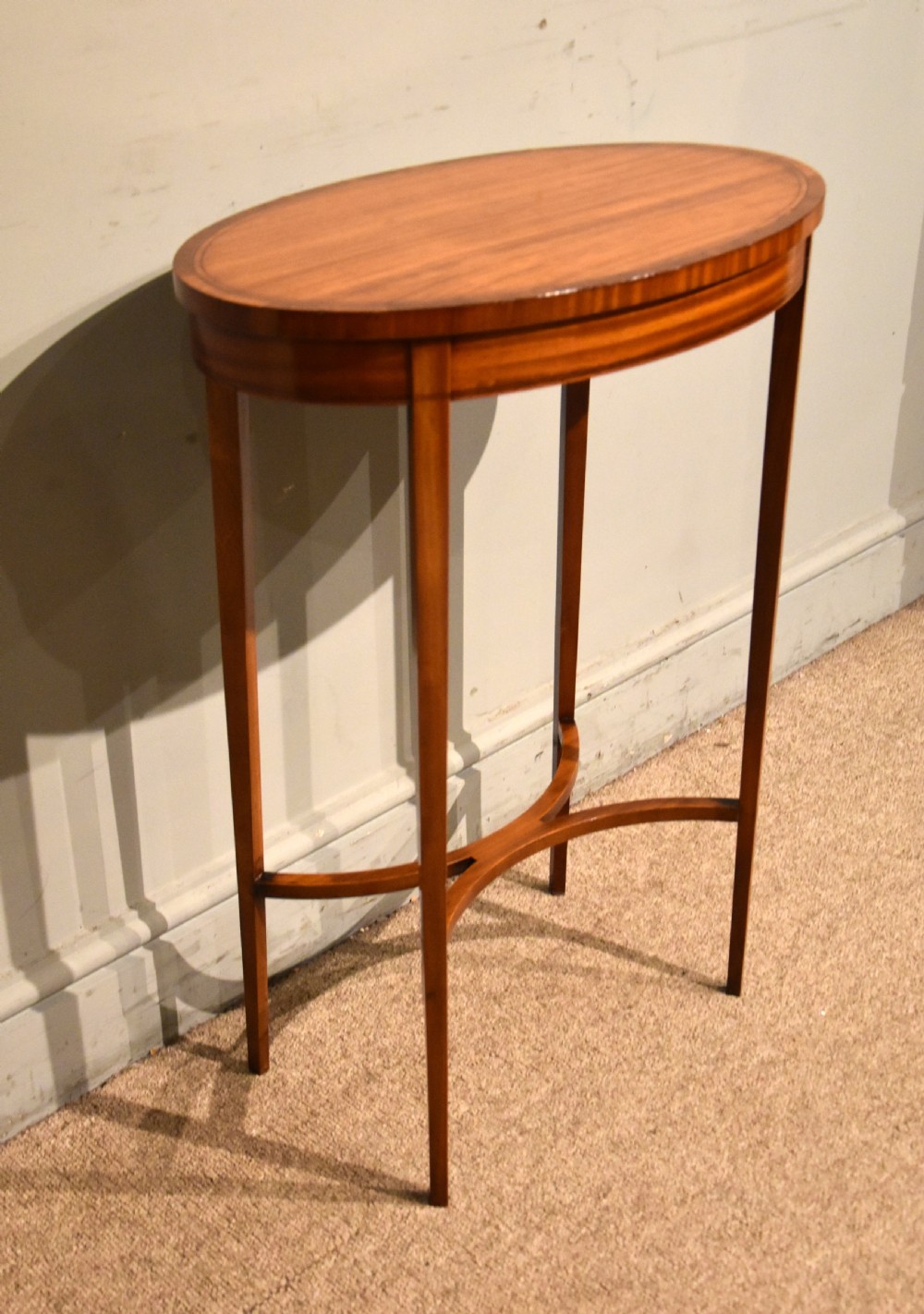 An oval Sheraton Revival occasional table crafted from satinwood with crossbanded border inlay, slender tapered legs, and a curved X-frame stretcher. View III