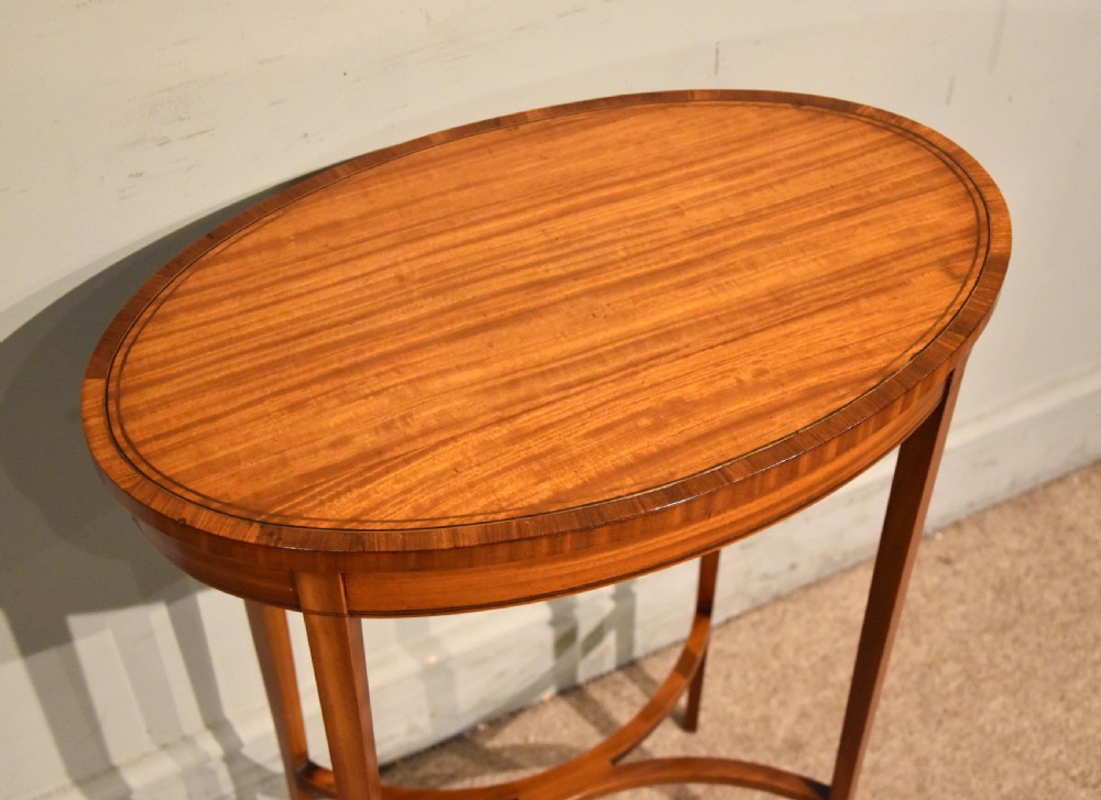 An oval Sheraton Revival occasional table crafted from satinwood with crossbanded border inlay, slender tapered legs, and a curved X-frame stretcher. View V