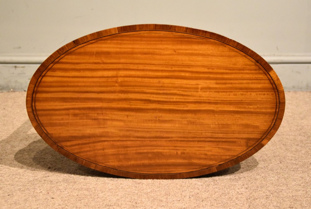 An oval Sheraton Revival occasional table crafted from satinwood with crossbanded border inlay, slender tapered legs, and a curved X-frame stretcher. View VI