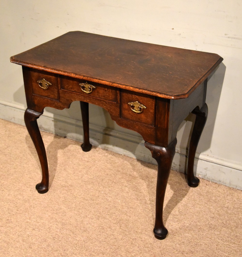 A mid-18th century dark oak lowboy featuring three drawers with brass handles, a shaped lower apron, and cabriole legs with pad feet.