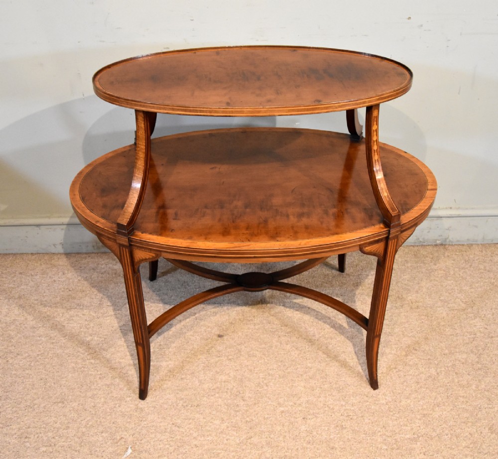 A two-tier mahogany oval etagere table featuring satinwood inlay, curved leg supports, and an X-shaped stretcher.