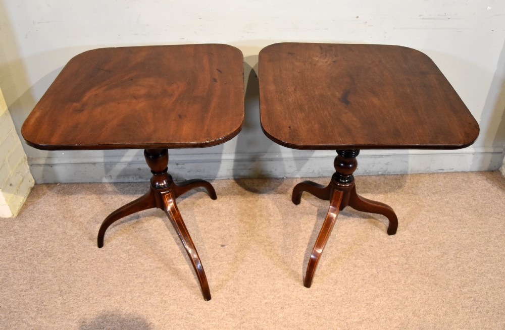 A matched pair of mahogany tripod tables featuring turned pedestals and square tops with rounded corners.
