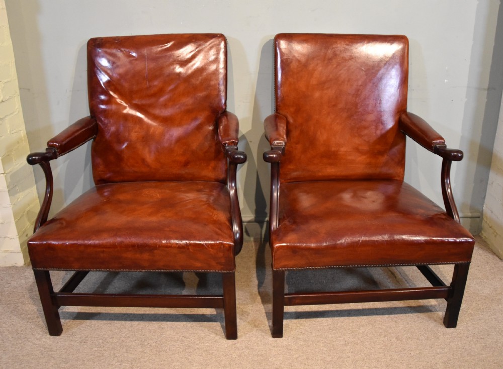 A pair of George III style mahogany armchairs with warm brown leather upholstery, padded open arms, and brass stud trim.