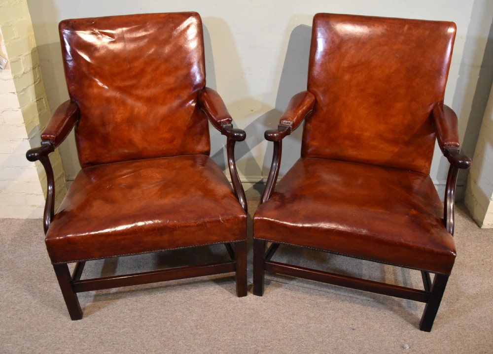 A pair of George III style mahogany armchairs with warm brown leather upholstery, padded open arms, and brass stud trim. View II