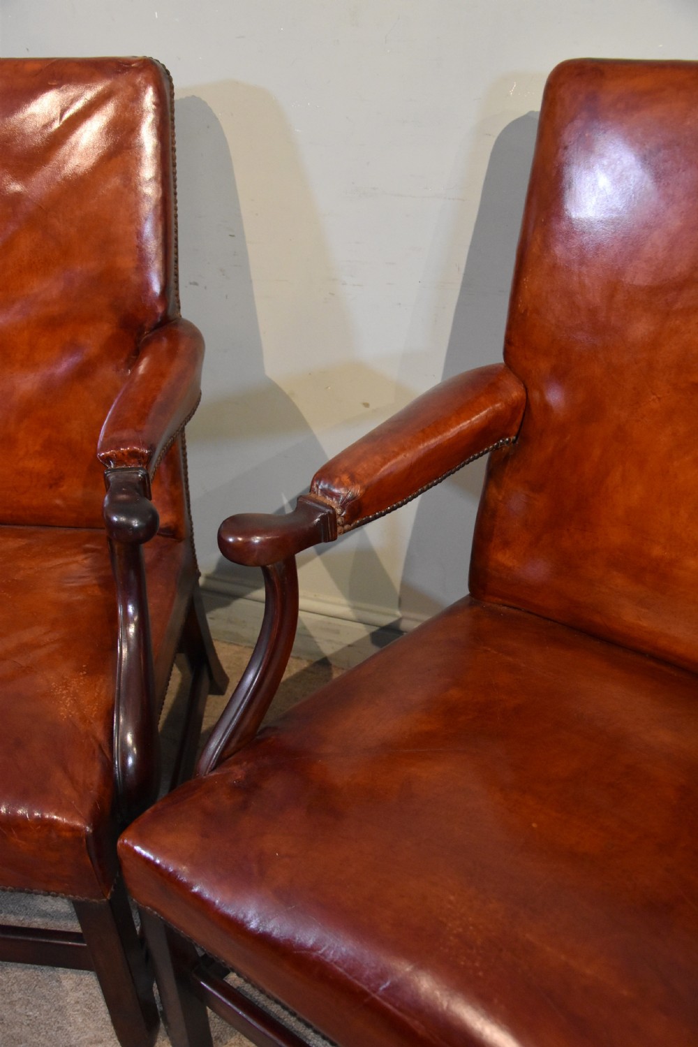 A pair of George III style mahogany armchairs with warm brown leather upholstery, padded open arms, and brass stud trim. View V