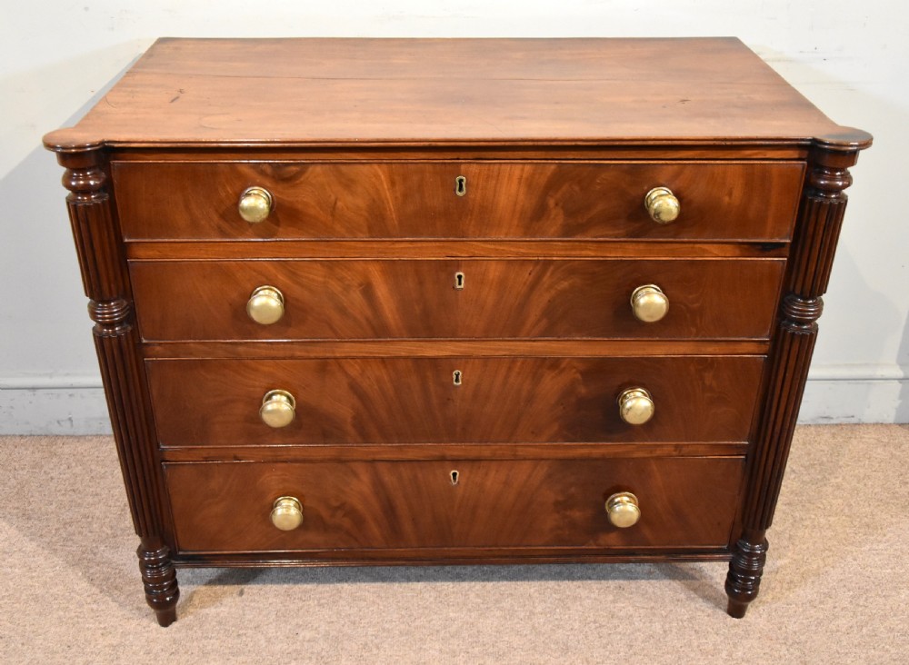 A Regency period mahogany chest of drawers featuring flame mahogany drawer fronts, turned brass knobs, and reeded side columns.