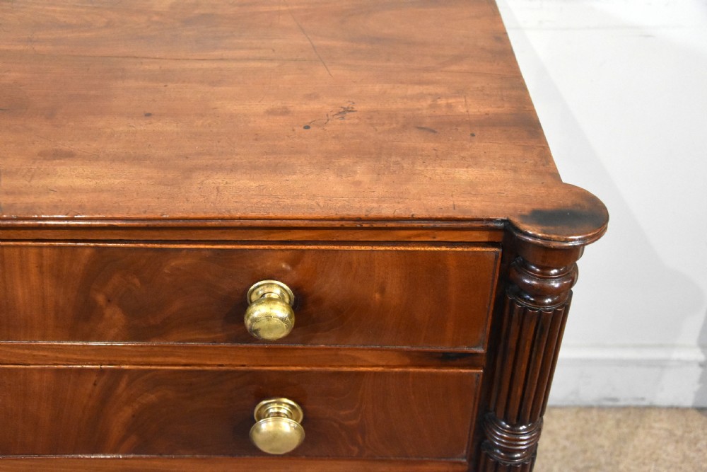 A Regency period mahogany chest of drawers featuring flame mahogany drawer fronts, turned brass knobs, and reeded side columns. View VII
