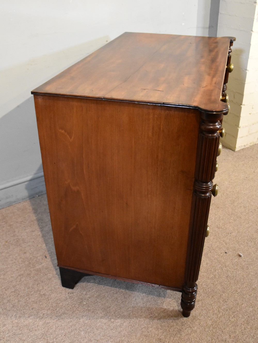 A Regency period mahogany chest of drawers featuring flame mahogany drawer fronts, turned brass knobs, and reeded side columns. View VIII