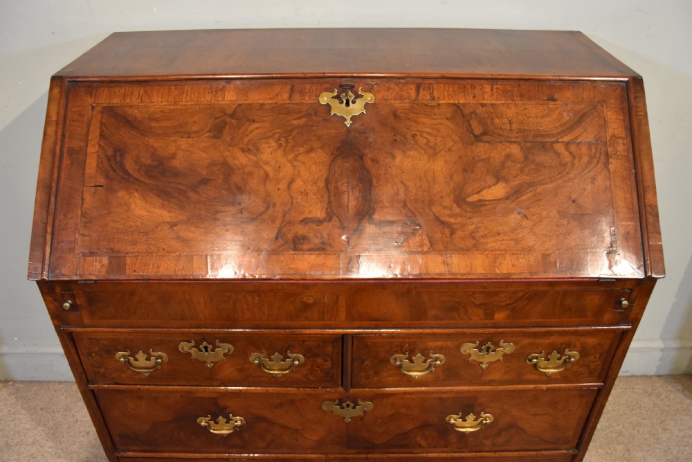 A George II walnut veneered bureau featuring a slant-front writing lid above four drawers with decorative brass handles and bracket feet. View III