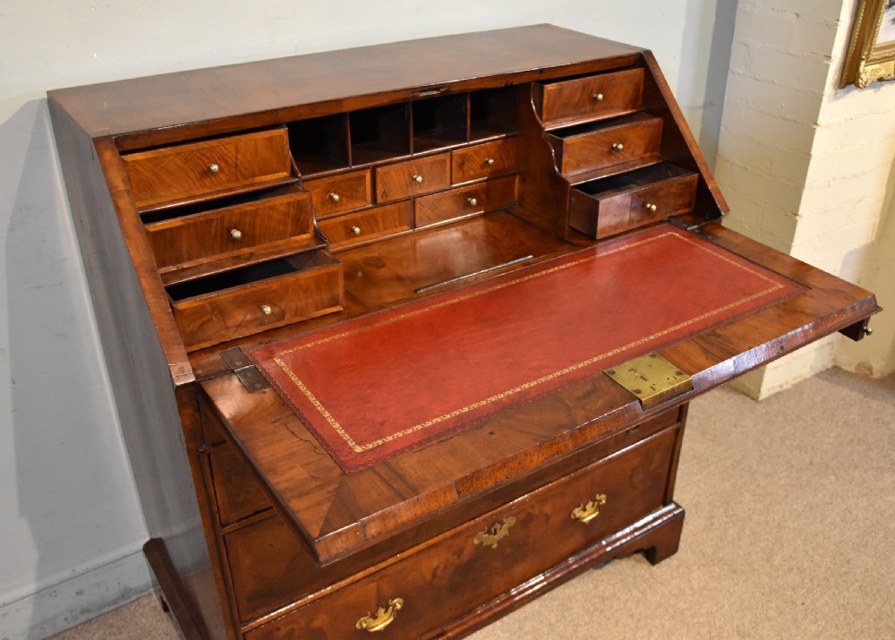 A George II walnut veneered bureau featuring a slant-front writing lid above four drawers with decorative brass handles and bracket feet. View IV