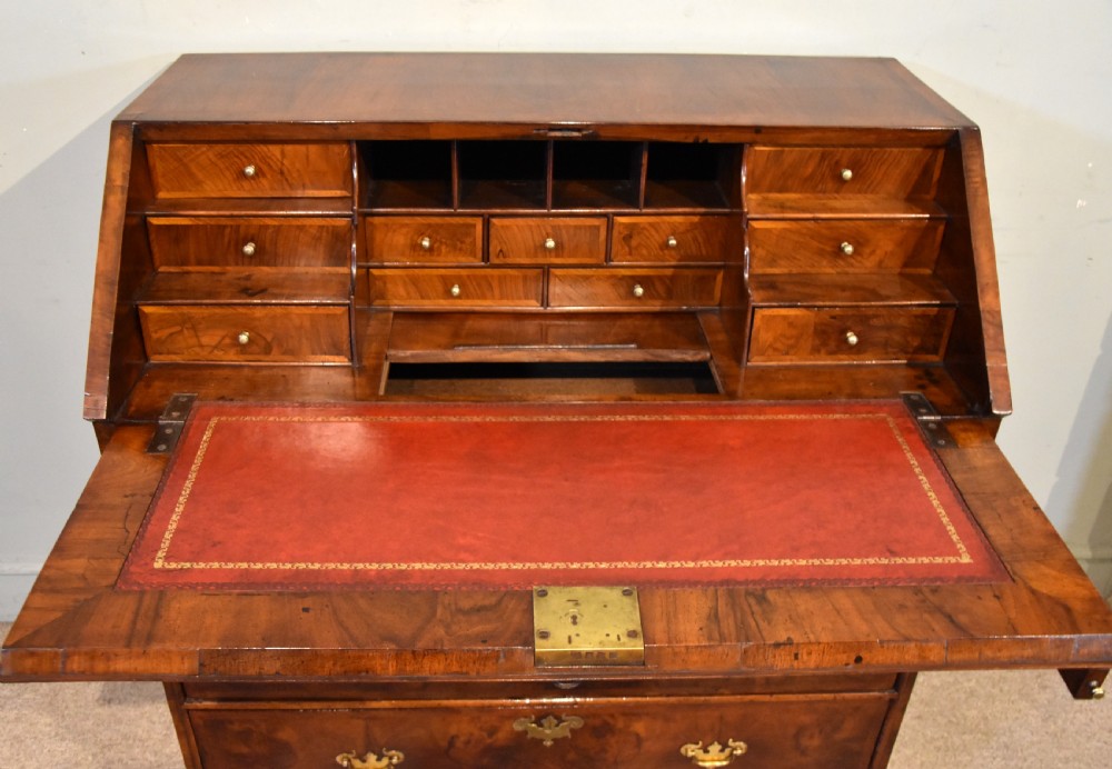 A George II walnut veneered bureau featuring a slant-front writing lid above four drawers with decorative brass handles and bracket feet. View V