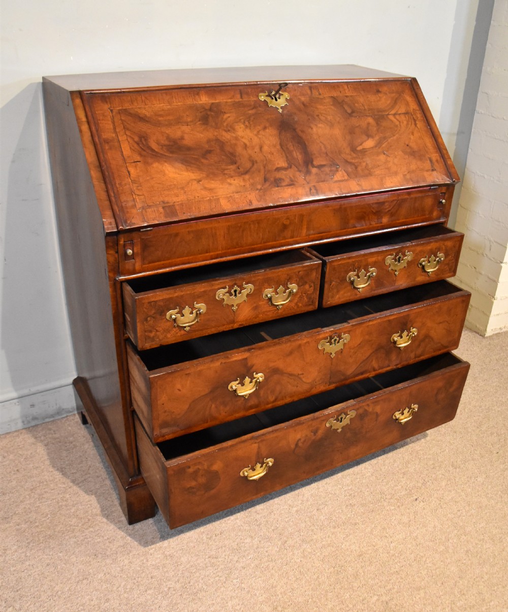 A George II walnut veneered bureau featuring a slant-front writing lid above four drawers with decorative brass handles and bracket feet. View VI