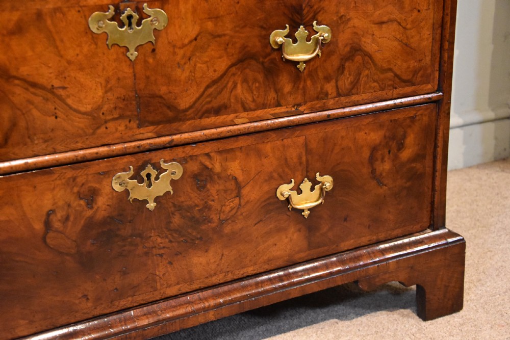 A George II walnut veneered bureau featuring a slant-front writing lid above four drawers with decorative brass handles and bracket feet. View X