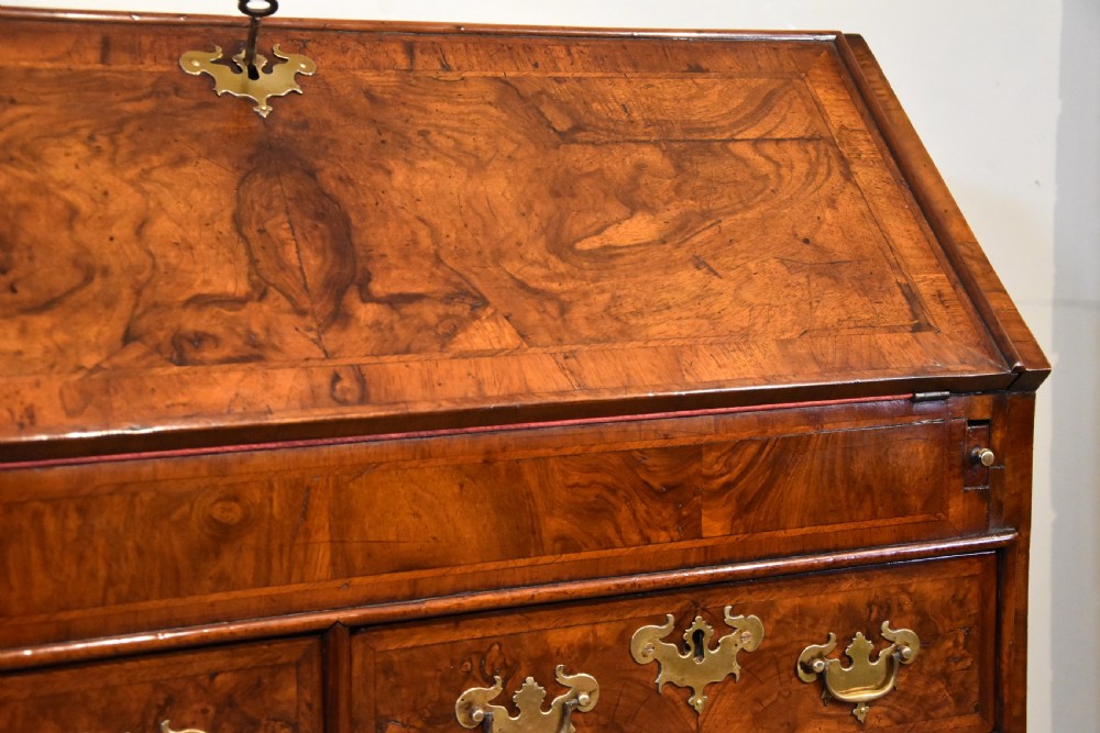 A George II walnut veneered bureau featuring a slant-front writing lid above four drawers with decorative brass handles and bracket feet. View XI