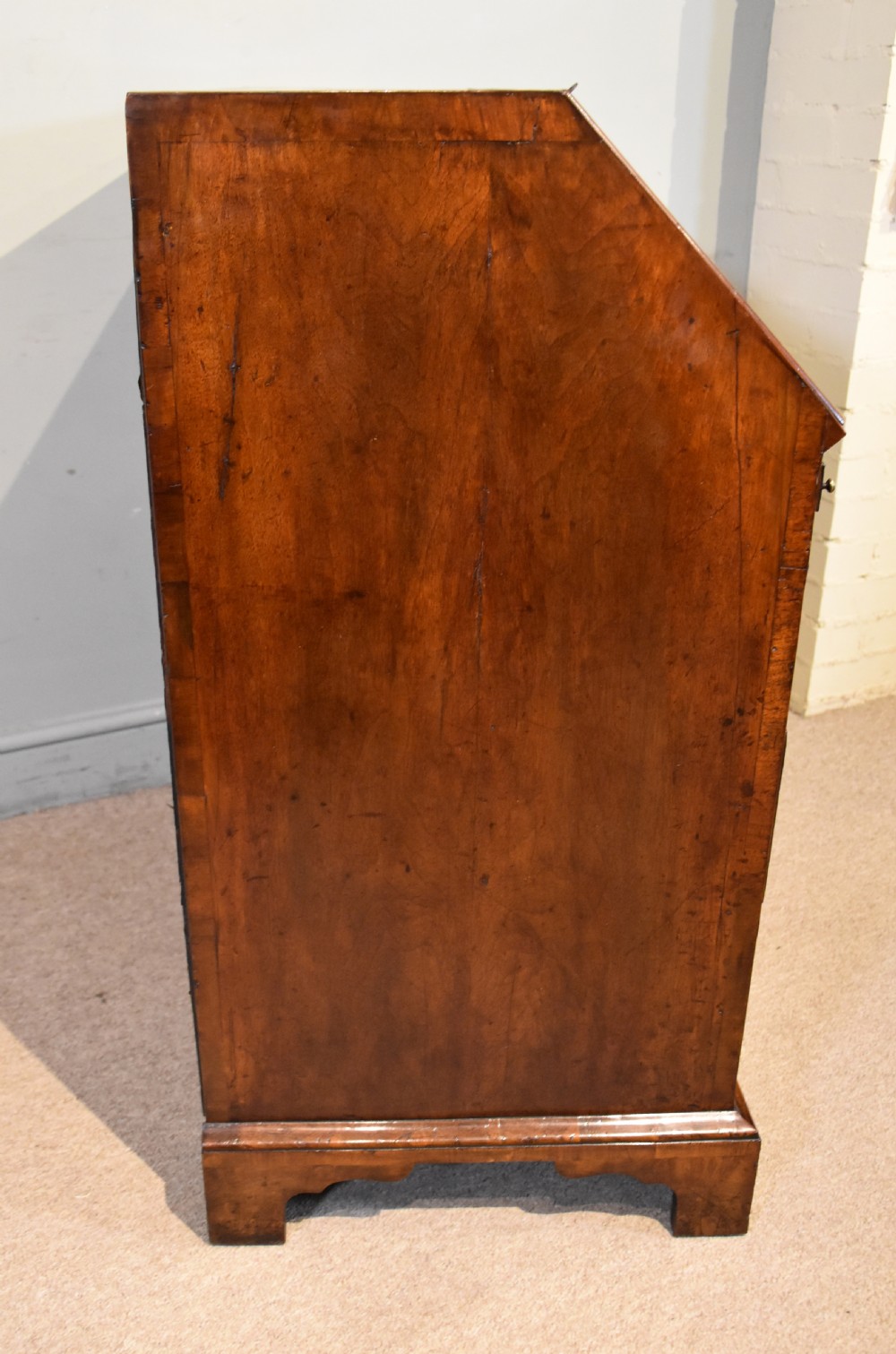 A George II walnut veneered bureau featuring a slant-front writing lid above four drawers with decorative brass handles and bracket feet. View XII