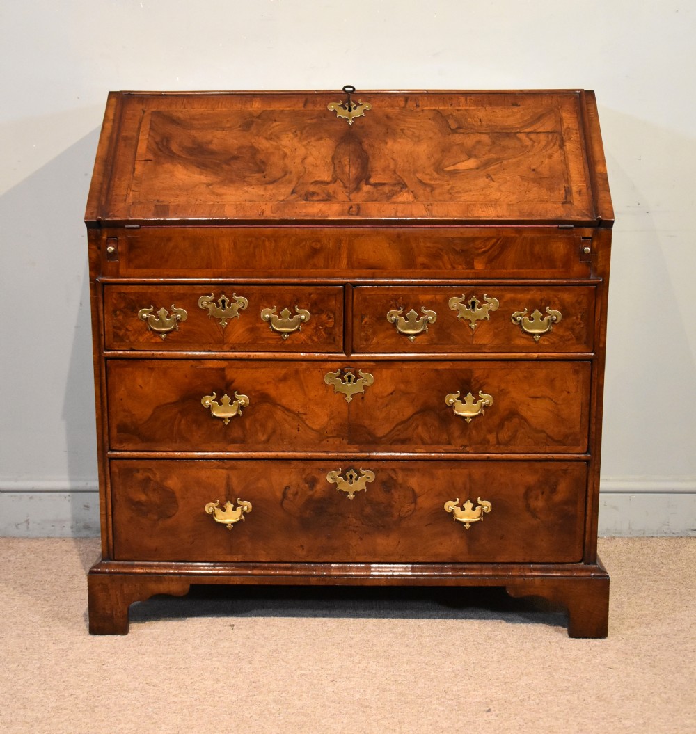 A George II walnut veneered bureau featuring a slant-front writing lid above four drawers with decorative brass handles and bracket feet.