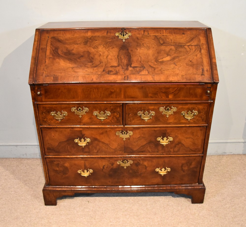 A George II walnut veneered bureau featuring a slant-front writing lid above four drawers with decorative brass handles and bracket feet. View II