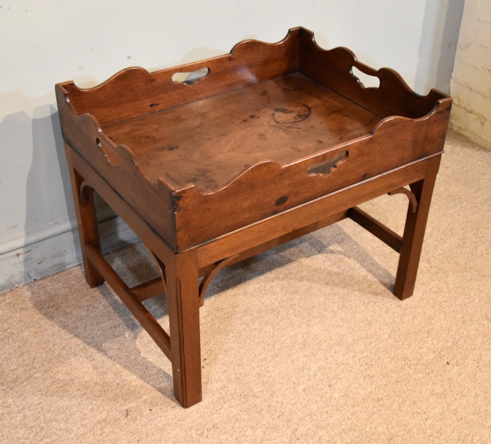 A mid-eighteenth-century mahogany butlers tray featuring scalloped gallery sides with cut-out handles, resting on a fitted rectangular wooden stand with corner spandrels.