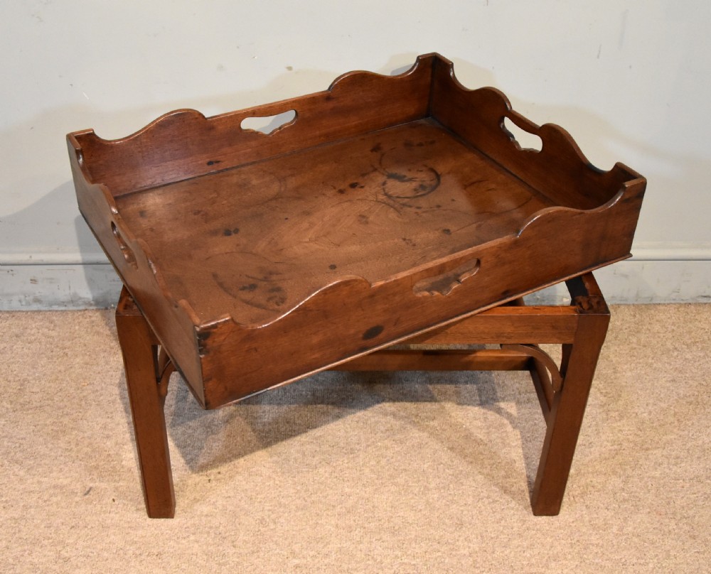 A mid-eighteenth-century mahogany butlers tray featuring scalloped gallery sides with cut-out handles, resting on a fitted rectangular wooden stand with corner spandrels. View V