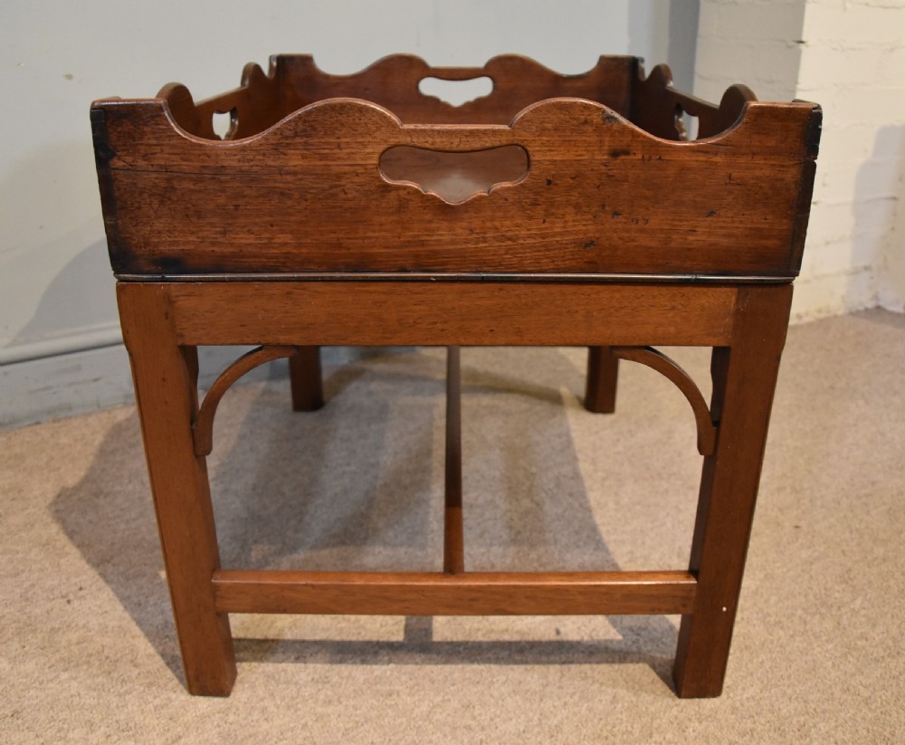A mid-eighteenth-century mahogany butlers tray featuring scalloped gallery sides with cut-out handles, resting on a fitted rectangular wooden stand with corner spandrels. View VII