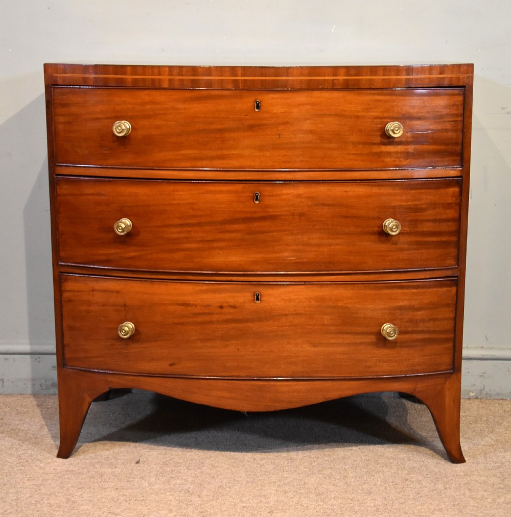 A Regency period mahogany bow-fronted chest featuring three full-width drawers with brass handles and splayed bracket feet.